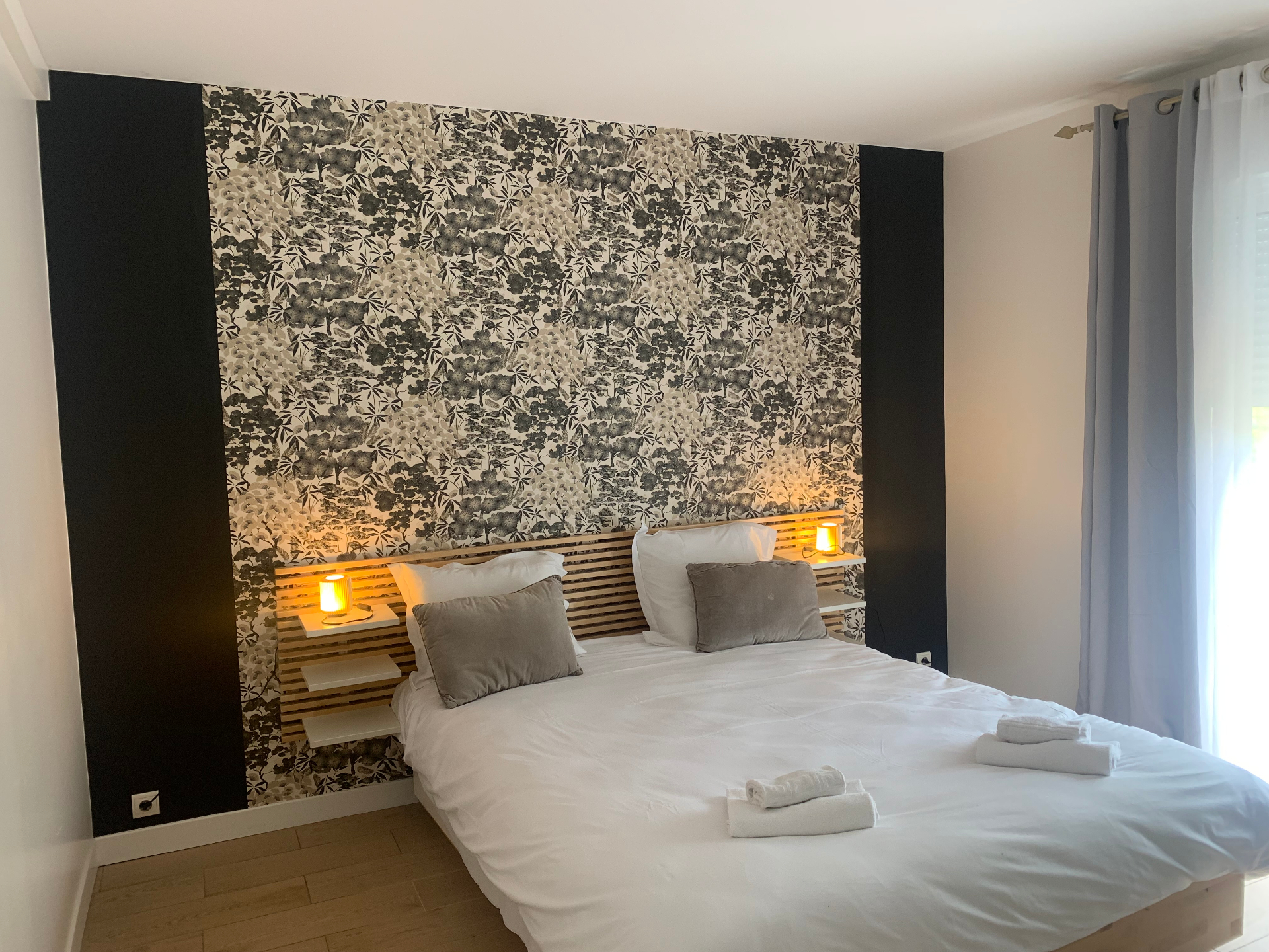 Première chambre double du F3 rez-de-jardin avec tête de lit en bois et papier peint floral
